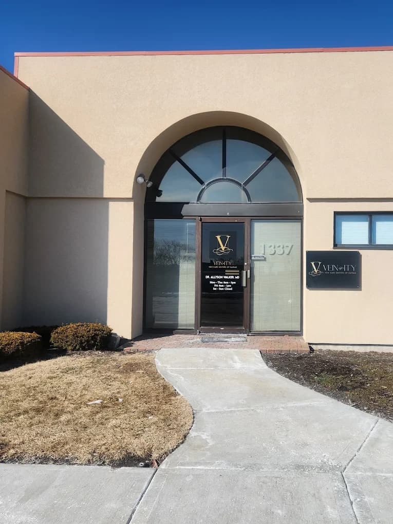 The entrance to Vein-ity: a stone building with an arched glass doorway carrying the practice's wordmark and the number 1337, reached by a concrete walkway.