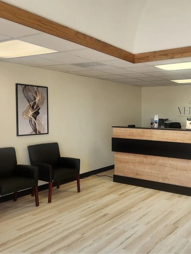 The Vein-ity waiting area: two black chairs below a framed abstract print in gold and gray, beside the reception desk and the practice's wordmark.