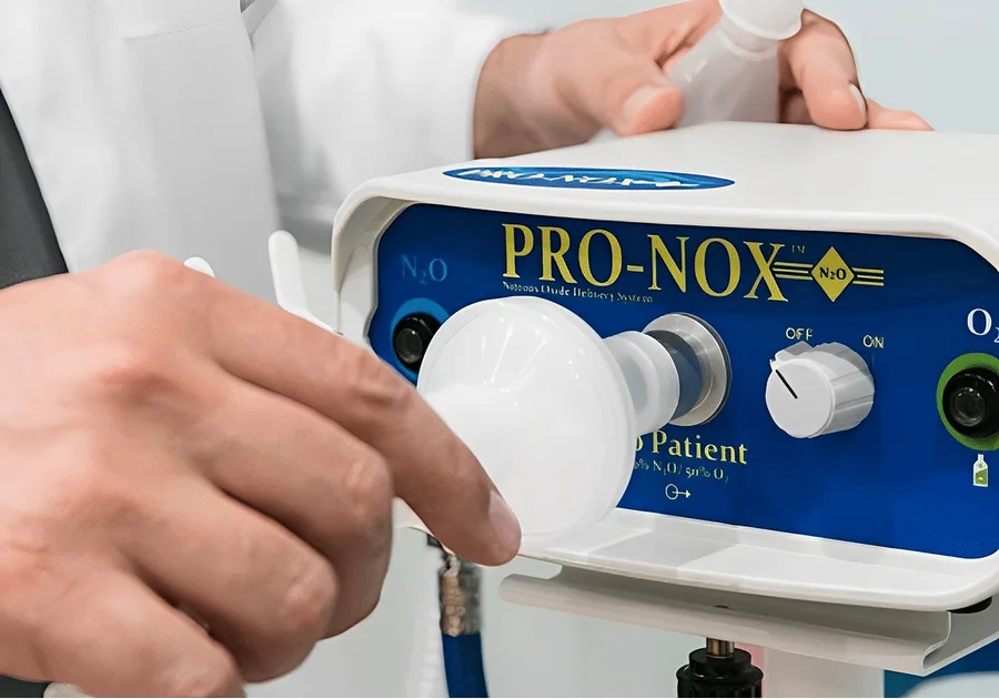 A clinician holding the mouthpiece of a Pro-Nox nitrous oxide delivery unit, its blue control panel showing the N2O and oxygen ports
