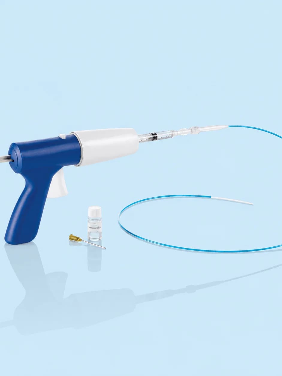 The VenaSeal delivery system on a plain blue background: a blue applicator with a trigger grip, a long coiled catheter, a small vial of medical adhesive and a dispenser tip.
