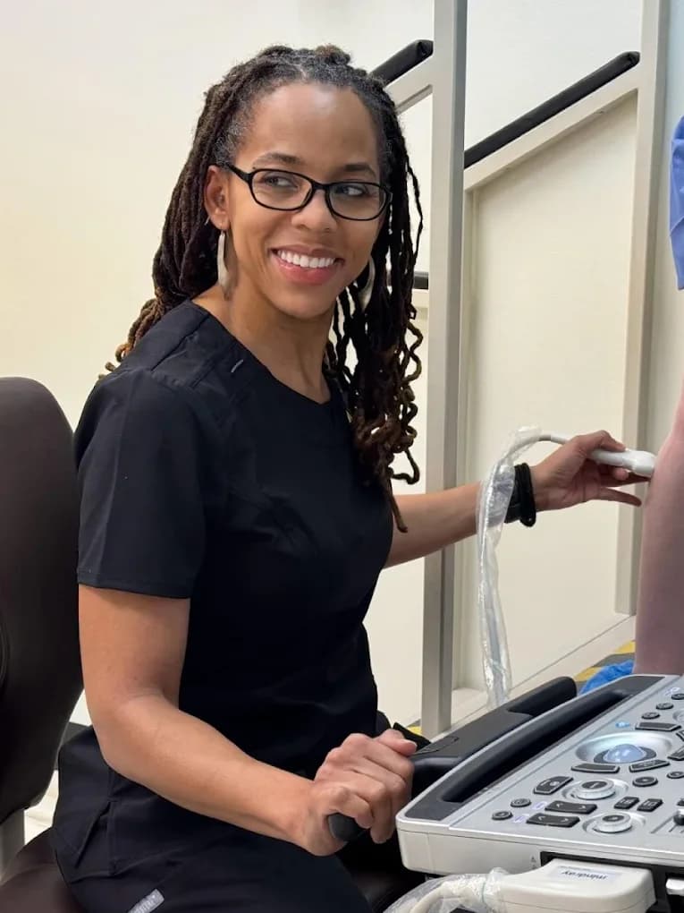 Dr. C. Allyson Walker seated at the ultrasound machine, one hand on the console and the other holding the probe against the leg of a standing patient.