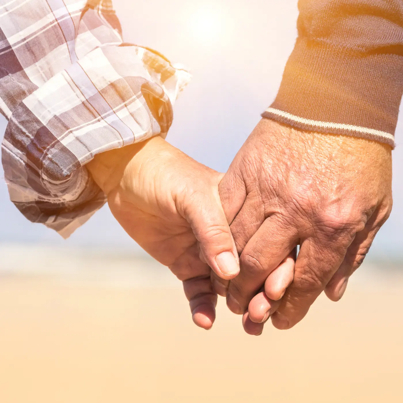 Two people holding hands outdoors in warm sunlight, the veins visible across the back of the older hand