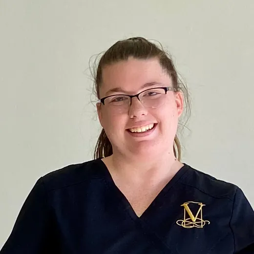 Maegan Cunningham sonriendo con lentes, con la casaca negra de Vein-ity y el monograma dorado.
