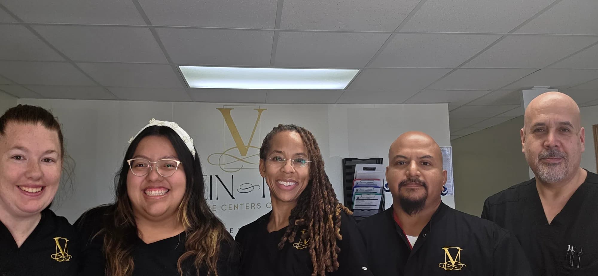 Cinco integrantes del equipo de Vein-ity sonriendo juntos en la clínica, frente al letrero dorado con la V de la práctica, con la Dra. C. Allyson Walker en el centro.